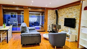 A modern living room with a sofa, armchair, and a TV. There is a fireplace and a dining area visible through a glass door. - Luxe studio Casa Angiz Etxea 2; charm, outdoor spa and valley views (Sunbilla)