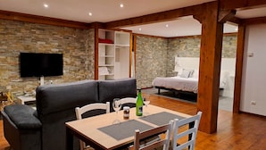 A modern living room with a stone wall, a flat-screen TV, a sofa, a dining table with chairs, and a bedroom with a bed and a nightstand. - Luxe studio Casa Angiz Etxea 2; charm, outdoor spa and valley views (Sunbilla)