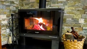 A wood-burning stove with a stone wall backdrop, a woven basket with logs, and a broom. - Luxe studio Casa Angiz Etxea 2; charm, outdoor spa and valley views (Sunbilla)