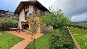 Una casa de dos pisos con fachada de piedra, un balcón y un patio con mobiliario exterior.