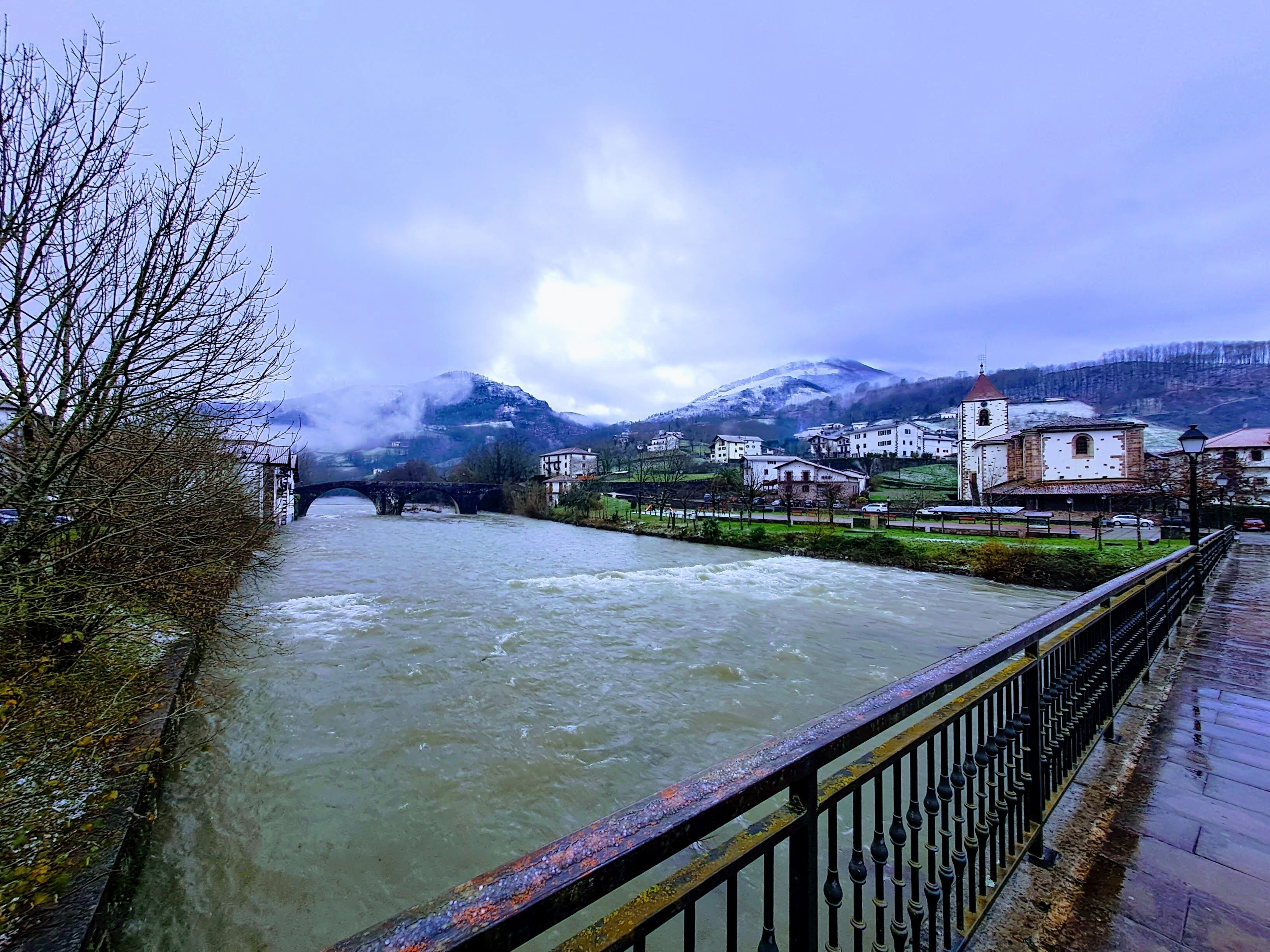 A river with a bridge, buildings, and mountains in the background.
