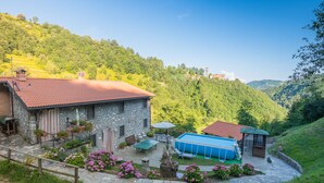 A stone house with a red-tiled roof, a swimming pool, and a patio with outdoor furniture.
