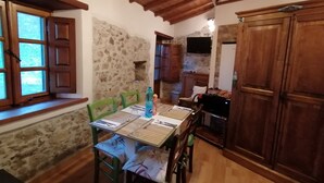 A rustic kitchen with stone walls, wooden cabinets, and a dining table set for four.