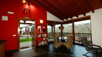 Une pièce avec un mur rouge, un plafond en bois, un balcon avec vue, des meubles en osier et un panneau indiquant « SORTIE ».