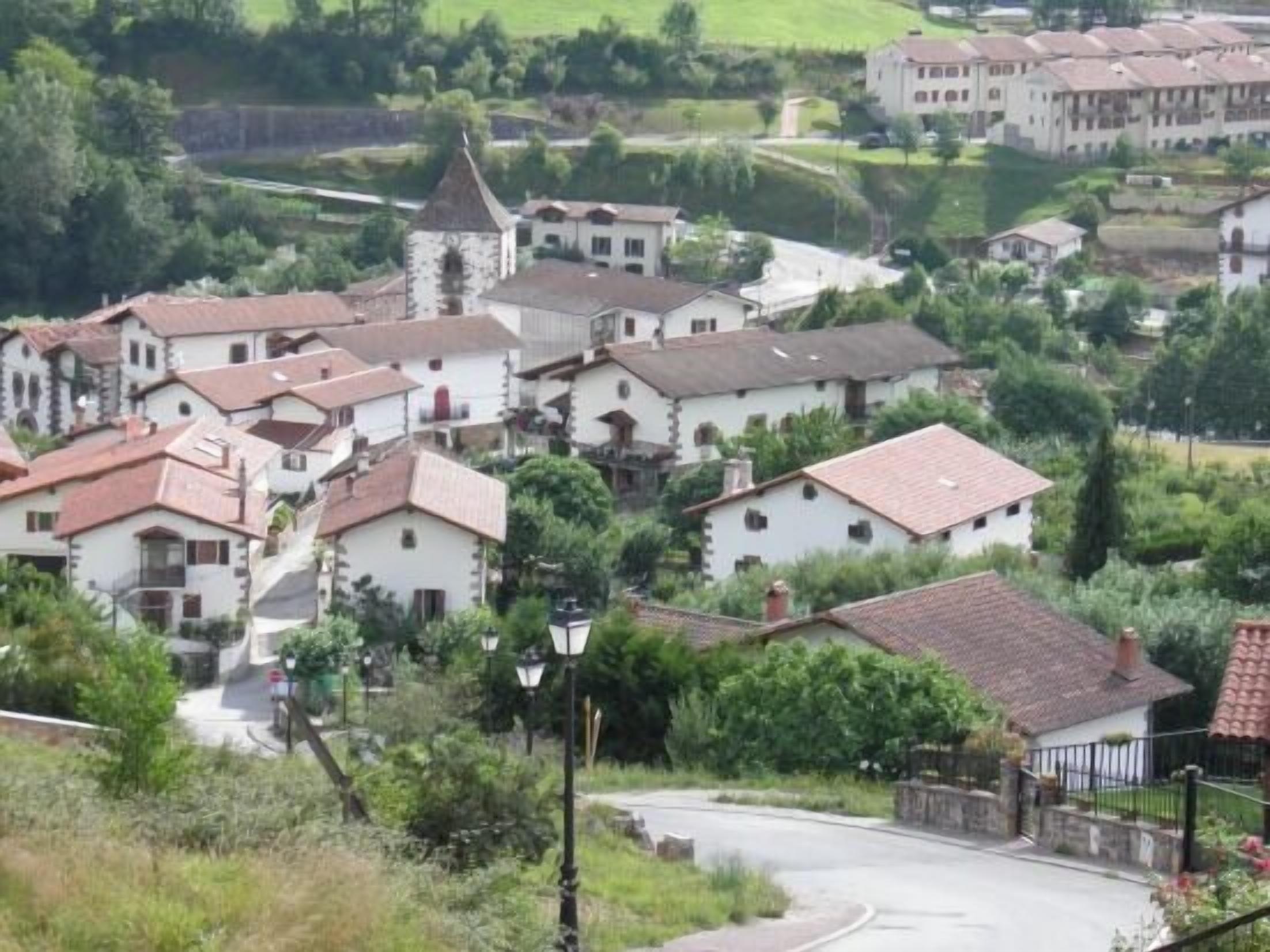 Un ensemble de bâtiments traditionnels aux murs blancs et aux toits de tuiles rouges, entourés de verdure et bordés d’une route sinueuse.