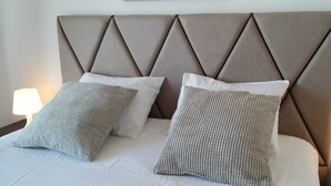 Un lit avec une tête de lit rembourrée, deux oreillers et des lampes de chevet.