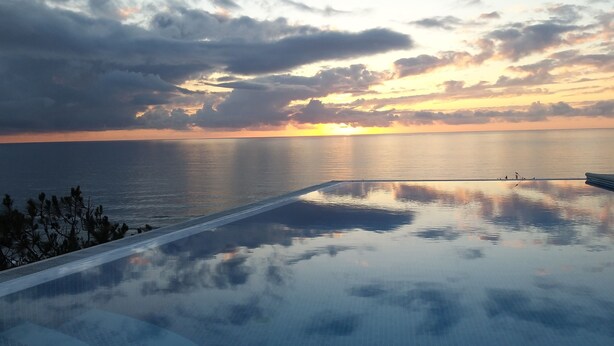 Une piscine à débordement offrant une vue sur l’océan et le coucher de soleil.