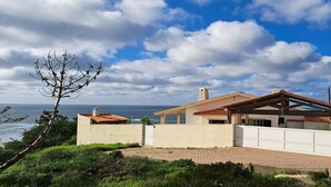 Une maison située sur la côte, avec vue sur l’océan, dotée d’un patio couvert et d’une entrée sécurisée par un portail.