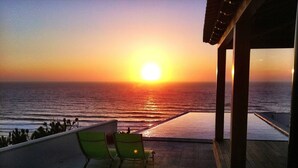 Une vue sur le coucher de soleil depuis un balcon, avec deux chaises et des plantes en pot.
