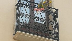 Un balcón con barandillas de hierro forjado y un arreglo floral.