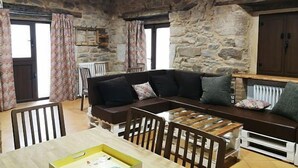 Un interior rústico de piedra con un banco, sillas y una mesa de madera.
