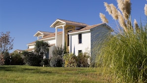 A two-story house with a tiled roof, surrounded by a well-maintained lawn and various shrubs. - Piscine Privée! Villa charmante proche du Golf (Moliets)