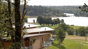 A cabin with a balcony overlooking a lake, surrounded by trees and a grassy area.