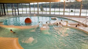 An indoor swimming pool with clear water, multiple entry points, and a view of a lake through large windows.