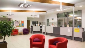 A reception area with a counter, red armchairs, a potted plant, and a bulletin board.