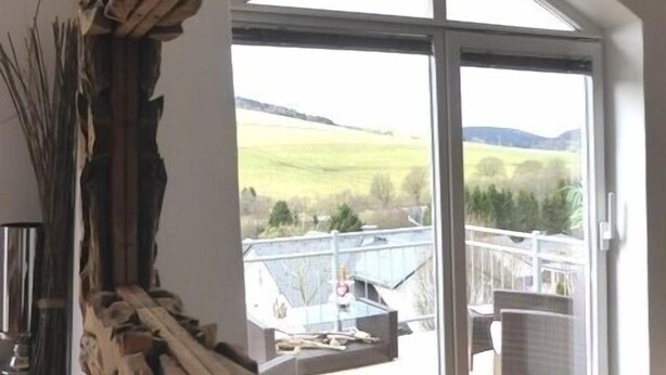A room with a large window offering a view of a green landscape and a bridge.