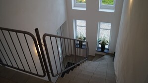 A staircase with a metal railing, leading to a landing with three windows offering views of greenery.