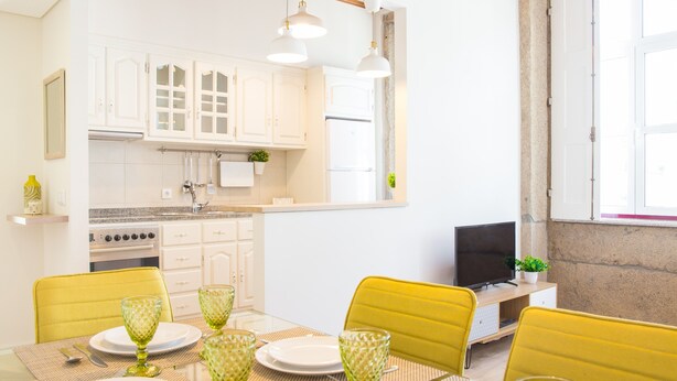 A modern kitchen with white cabinets, a built-in oven, and a dining area with yellow chairs and green glassware. - Spacious 3BR / 2 bath | Historic center Braga (Braga)
