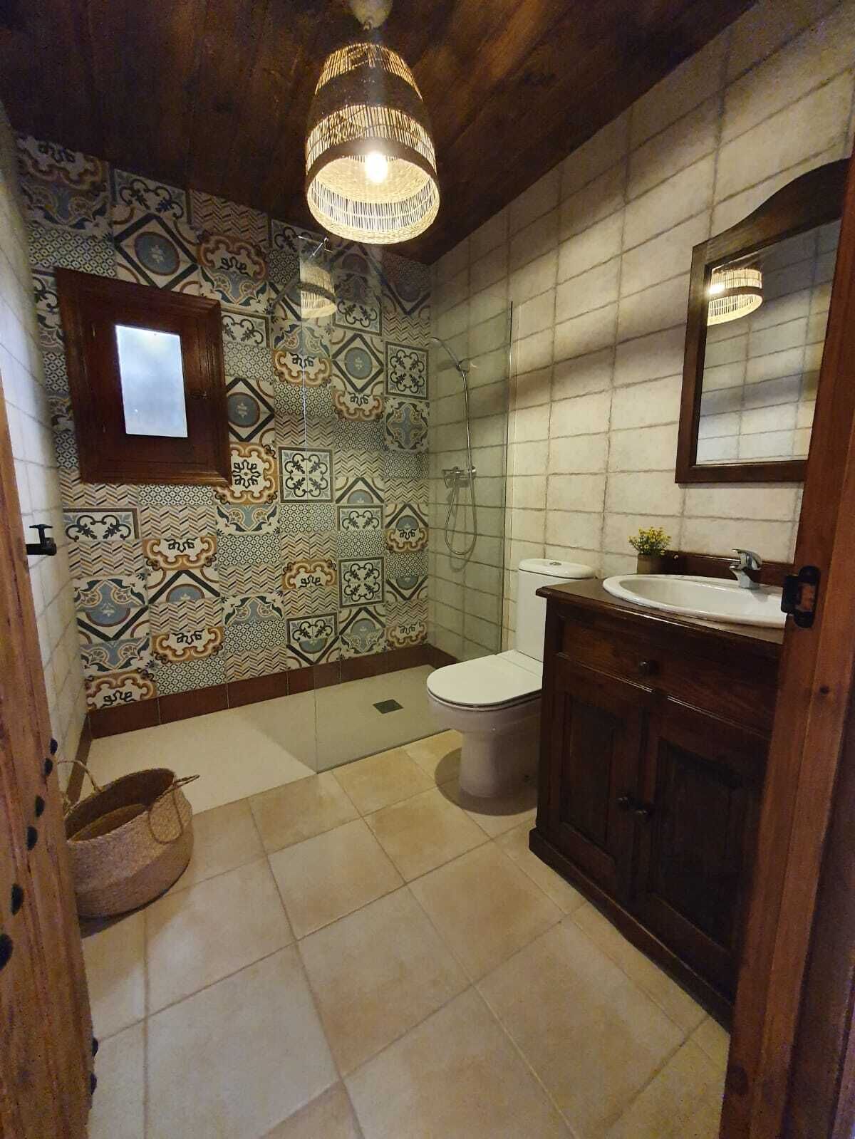A bathroom with patterned tiles, a toilet, a sink, and a wooden cabinet.
