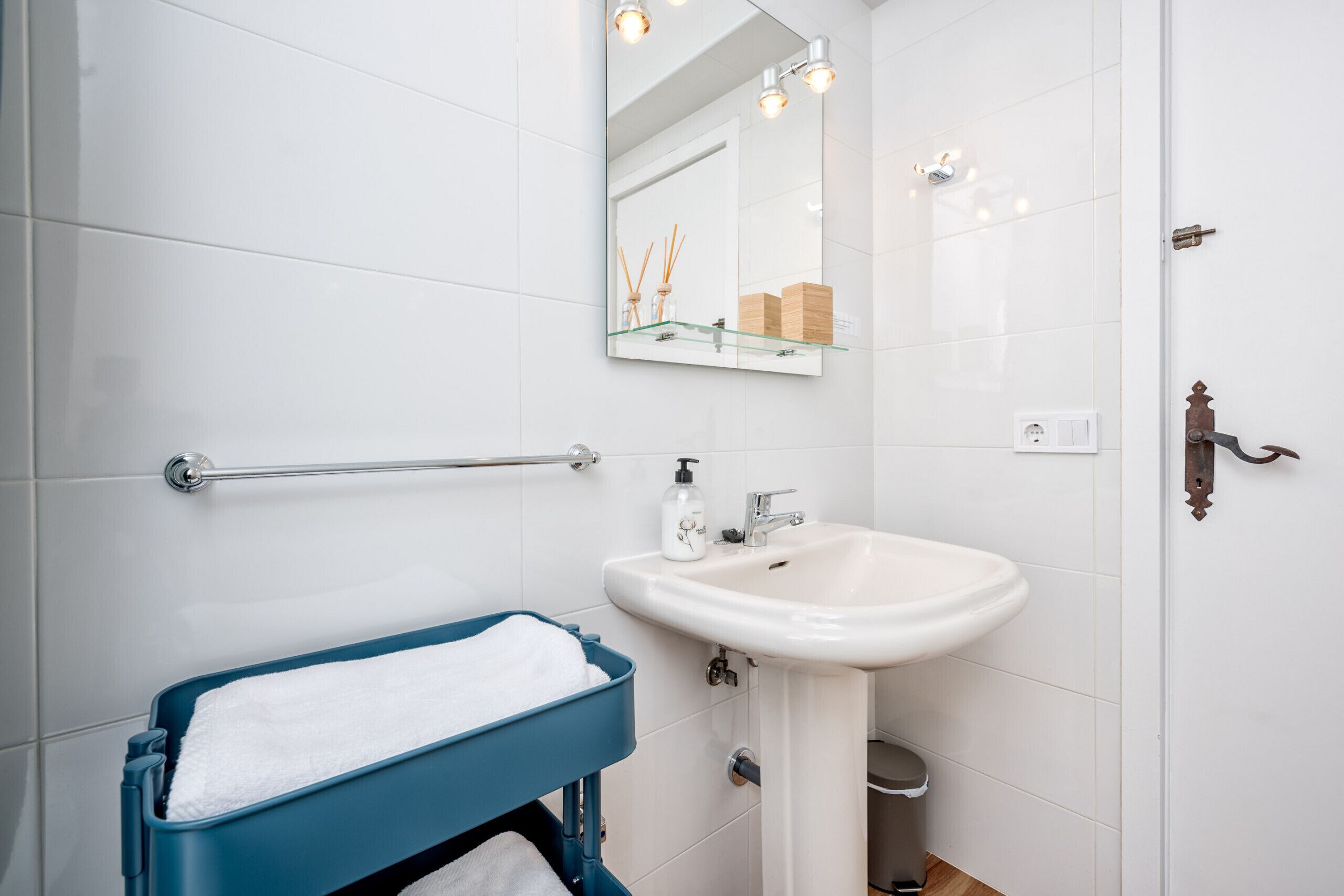 Un baño con un lavamanos blanco, un espejo y un perchero azul.