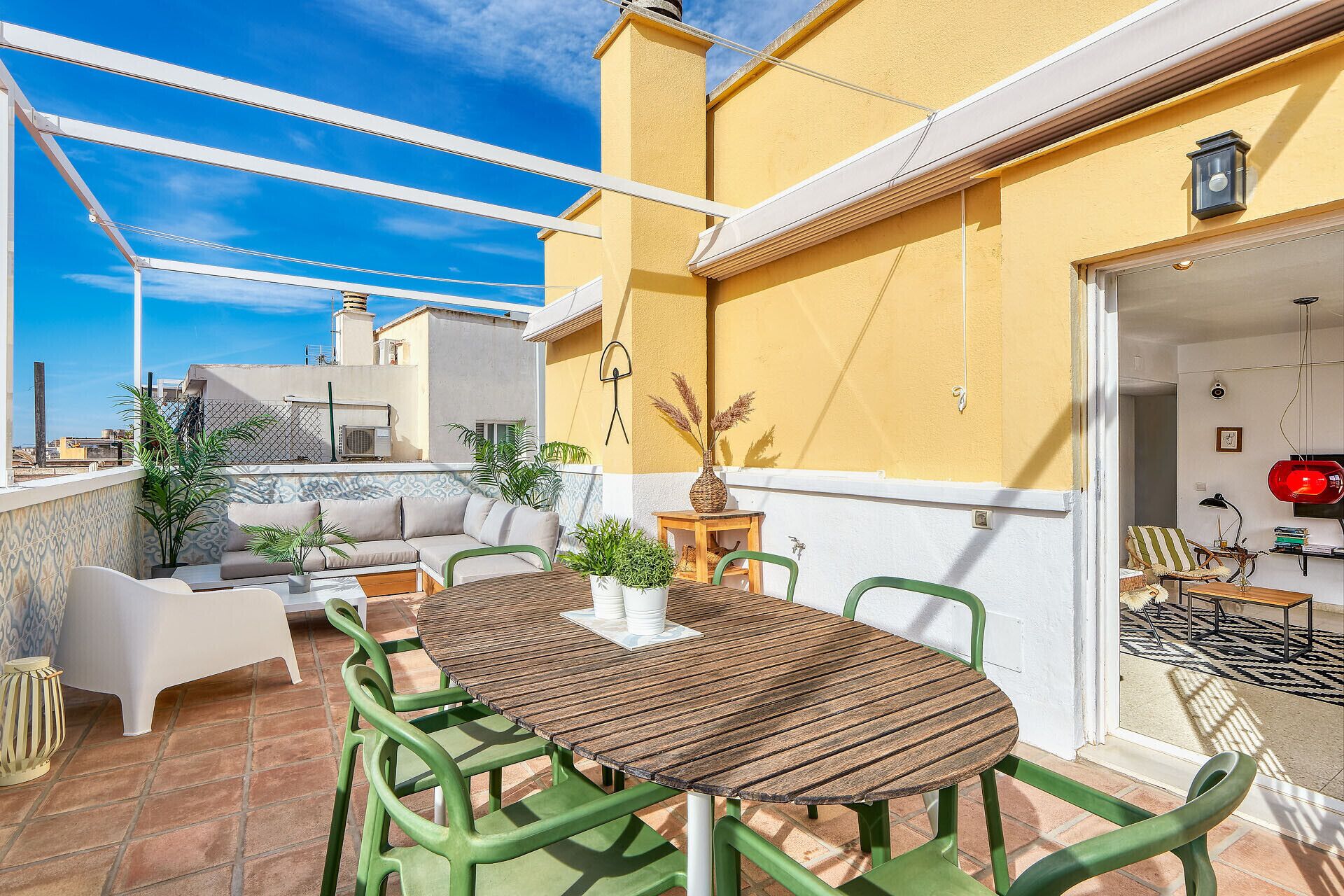 Una terraza con mesa y sillas de madera, un sofá y plantas en macetas.