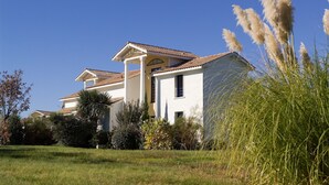 A two-story house with a tiled roof, surrounded by a well-maintained lawn and various shrubs.