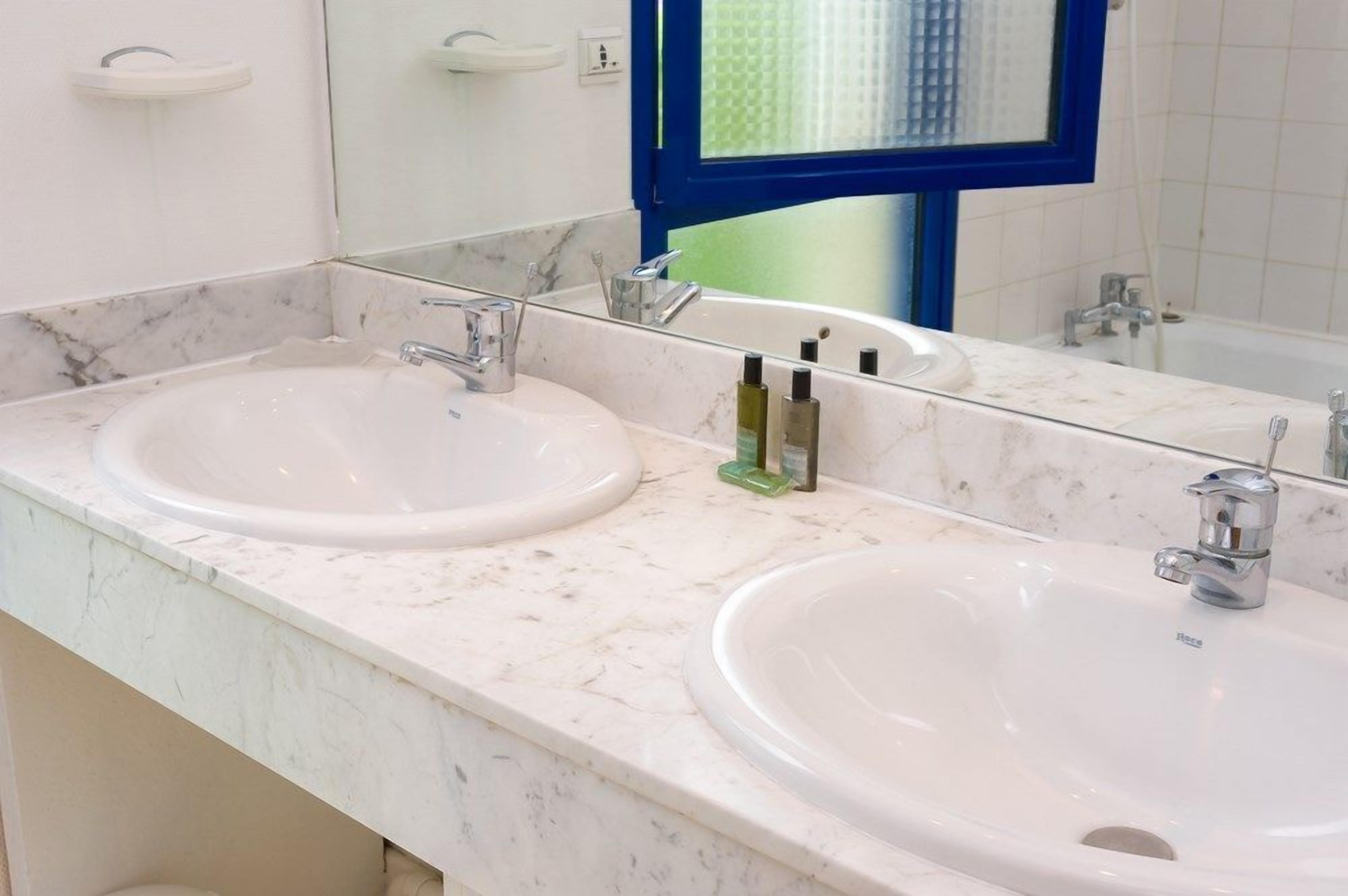 A bathroom with two sinks, a mirror, and a window with a blue frame.