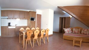 A dining area with wooden chairs and a table, a kitchen with wooden cabinets and appliances, and a loft bedroom with a bed and window.