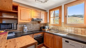 A compact kitchen with wooden cabinets, a microwave, a coffee maker, and a dishwasher. - Chalet avec cheminée | Accès direct aux pistes ! (Huez)