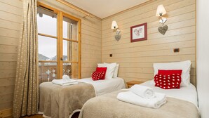 A room with two beds, each with a red heart-patterned pillow and a white towel. There are wall-mounted lamps and a framed picture on the wall. - Chalet avec cheminée | Accès direct aux pistes ! (Huez)