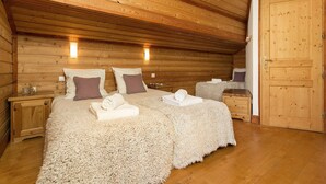 A cozy wooden cabin bedroom with two beds, a large fluffy rug, and a wooden door. - Chalet avec cheminée | Accès direct aux pistes ! (Huez)