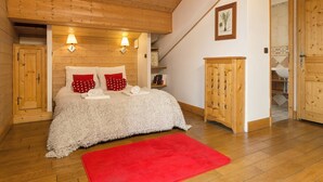 Un dormitorio con techo de madera, una cama con ropa de cama blanca y almohadas rojas, una alfombra roja y armarios de madera.