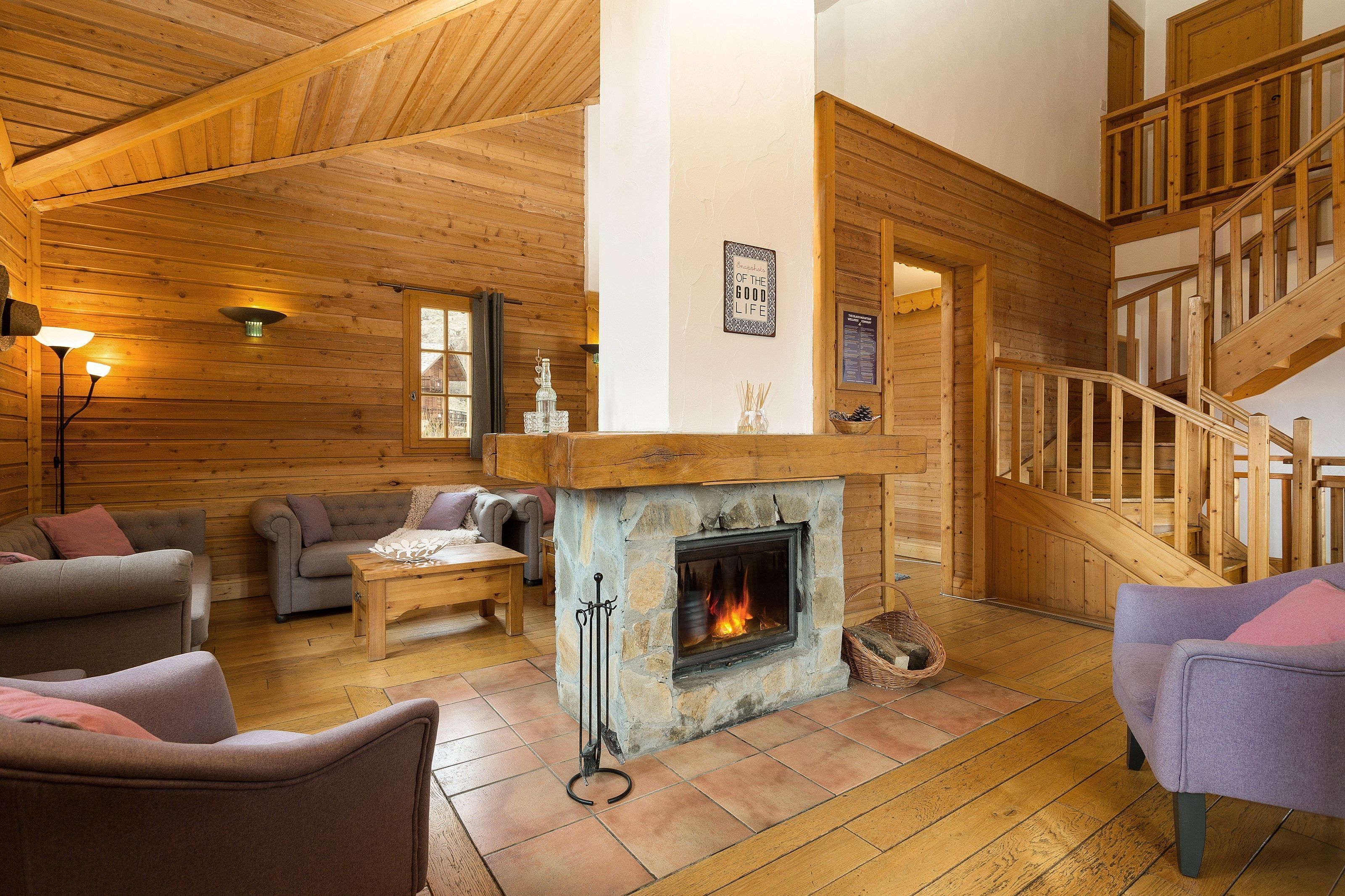 A cozy log cabin interior with a stone fireplace, wooden staircase, and comfortable seating areas.