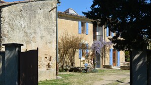 Ein rustikales Gebäude mit einer Stein-Fassade, einem Holztor und einem Weg, der zu einem Haus mit blauen Fensterläden und einem Garten mit blühenden Blumen führt.