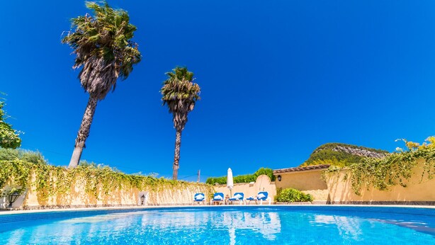 Una piscina azul cristalina con sillas de descanso y palmeras.