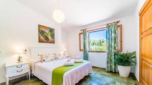 Un dormitorio con cama, mesitas de noche, un cuadro, una ventana con cortinas y una planta en maceta.