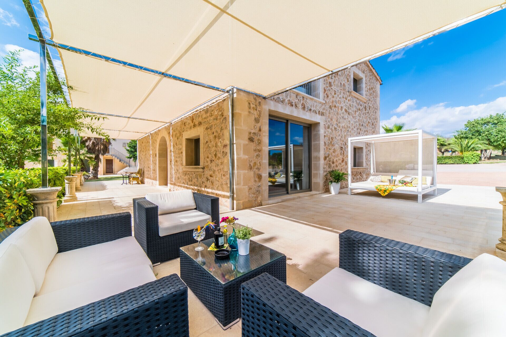 An outdoor patio area with wicker furniture, a covered seating area, and a stone building with a glass door.