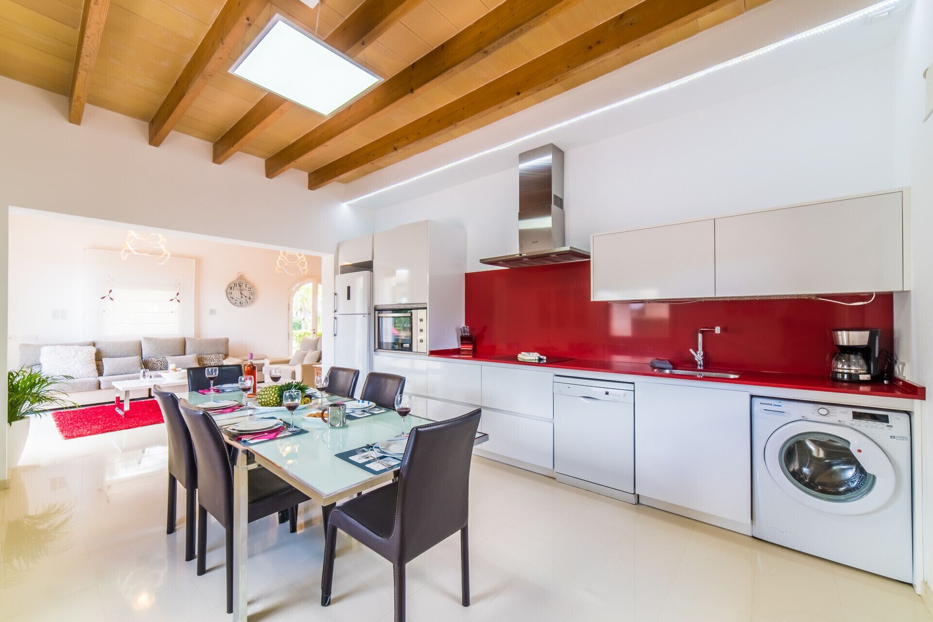 Une cuisine moderne avec des meubles blancs, un pare-feu rouge et un lave-linge encastré.