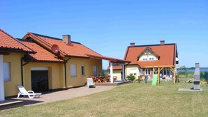 Ein zweistöckiges Haus mit rotem Ziegeldach, einer Terrasse mit Liegestühlen und einer kleinen Spielanlage.