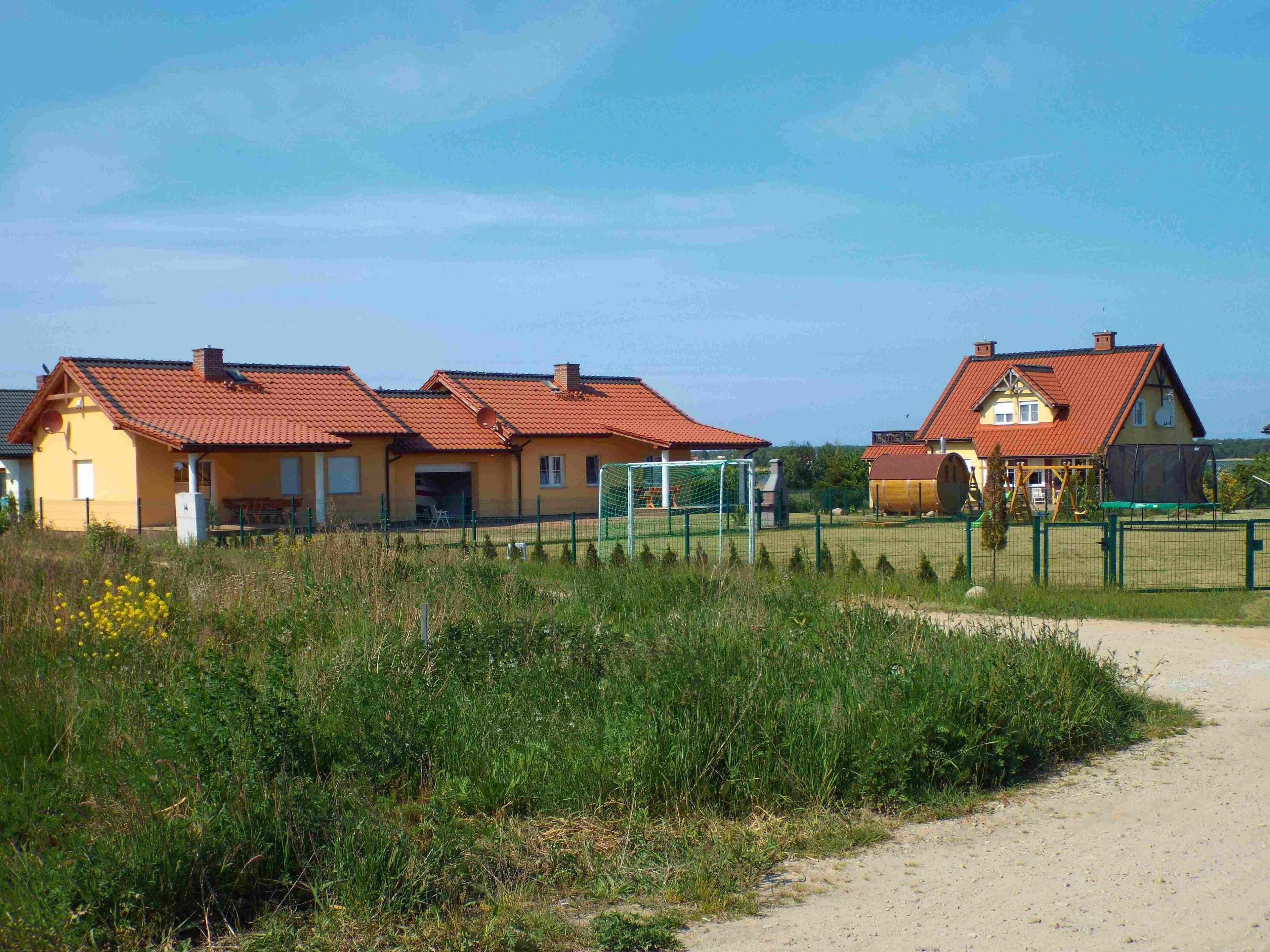 Række af huse med røde tagsten og en jordvej, der fører hen til et fodboldmål.