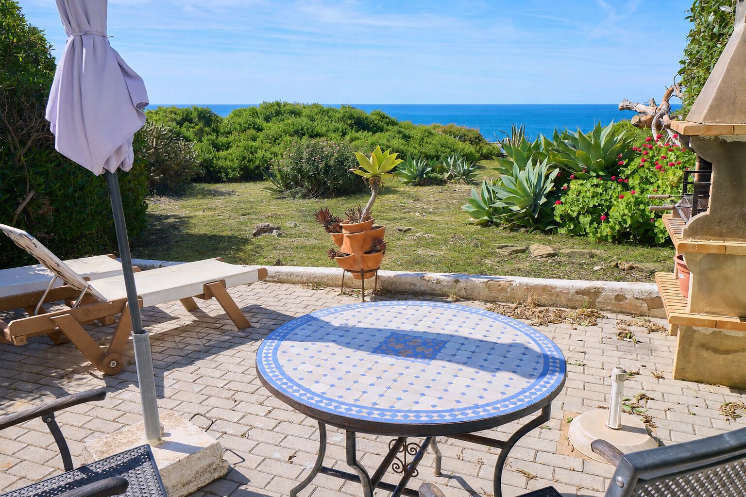 Eine Terrasse mit einem runden Tisch, einem Liegestuhl und Blick auf das Meer.