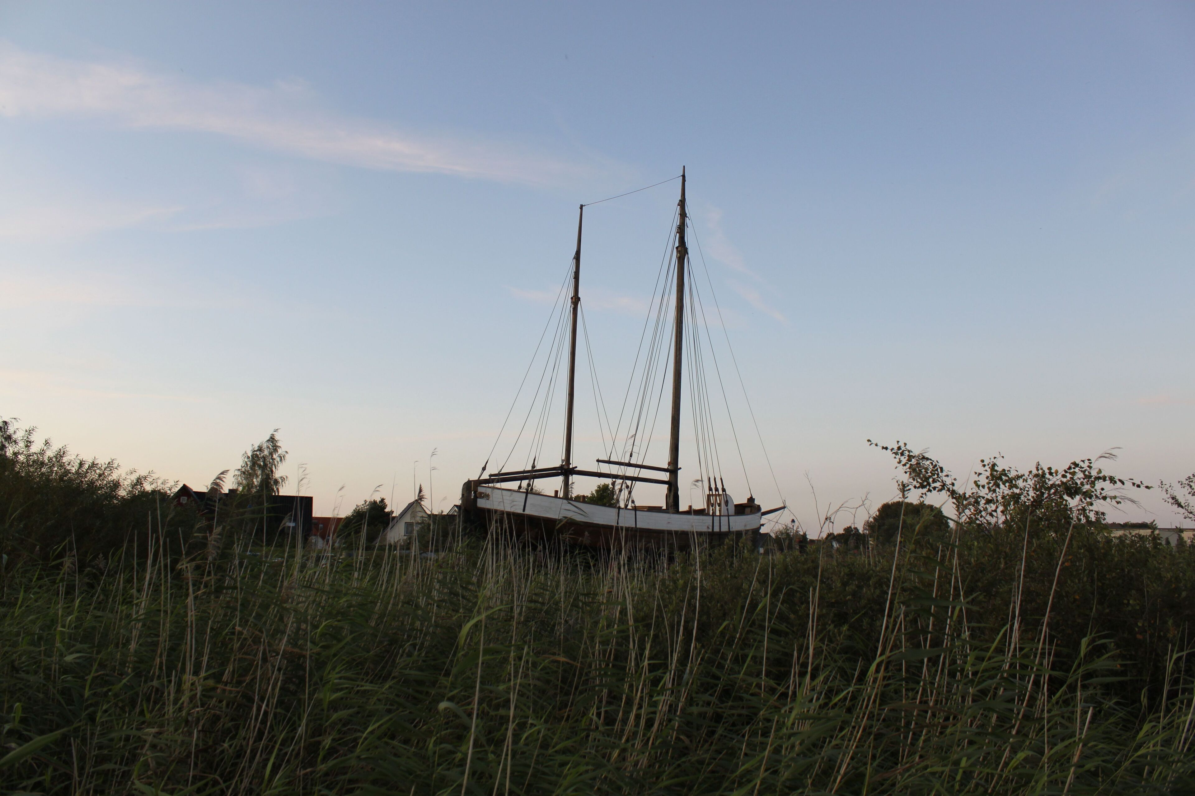 A sailboat docked in a grassy area with a clear sky.