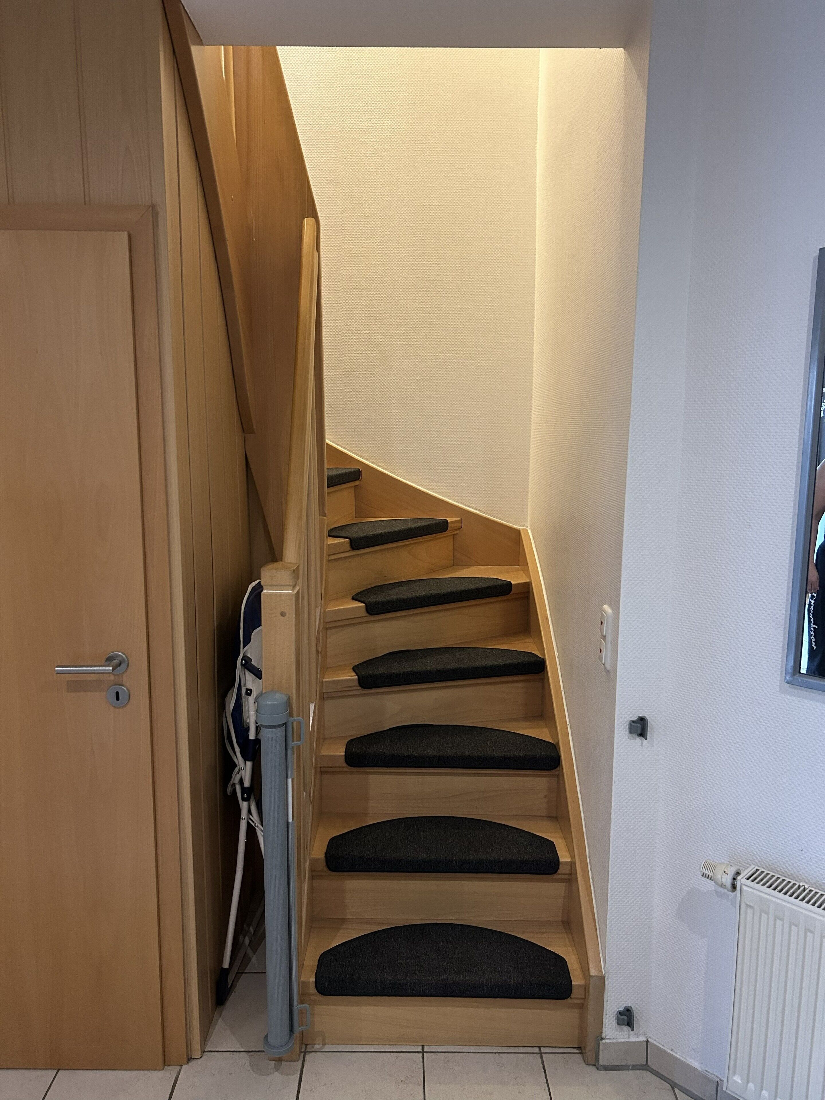 Un escalier en bois, avec des marches recouvertes de moquette noire, menant à un palier.