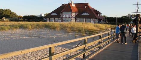 A wooden boardwalk leading to a building with a red roof and large windows.