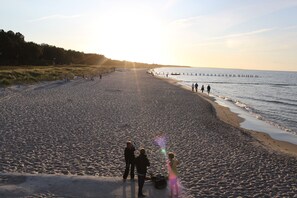 Una platja ampla amb una corba suau, un moll que s'endinsa a l'aigua, i gent passejant al costat de la riba.
