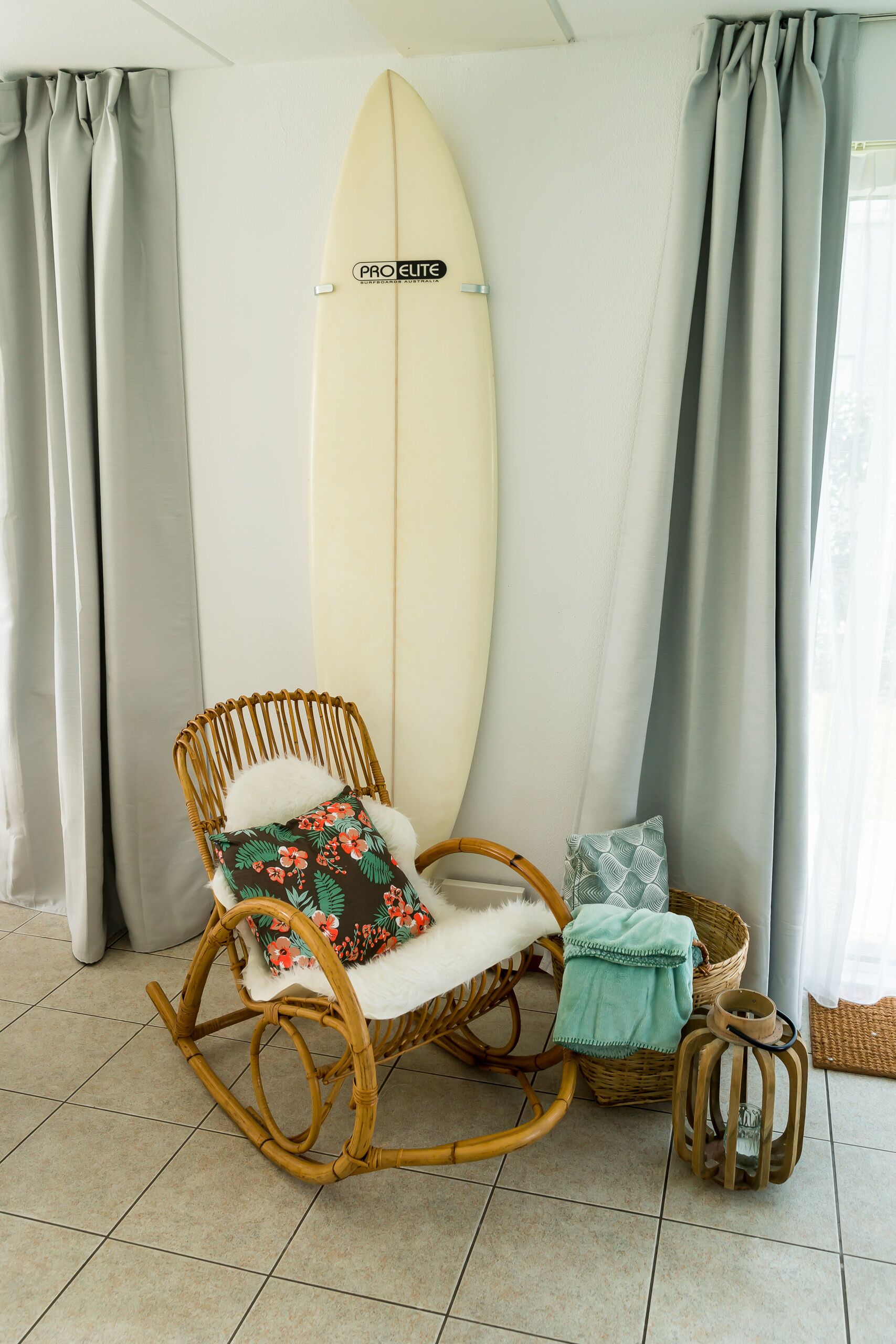 Una stanza con un surfboard, una sedia a dondolo in vimini e un tavolino con un bicchiere.