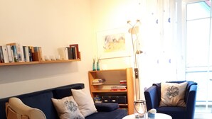 Un salon avec un canapé bleu, une chaise en bois, une petite table ronde et une bibliothèque.