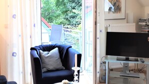 Un salon avec un fauteuil bleu foncé, une table ronde blanche ornée d’une bougie et un téléviseur posé sur un meuble en verre.