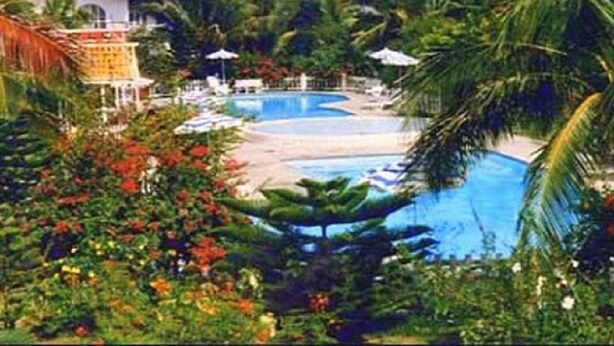 Een resort met een groot zwembad, palmbomen en een strand.
