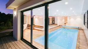 Une piscine moderne avec des portes vitrées donnant sur une terrasse en bois et un intérieur lumineux.